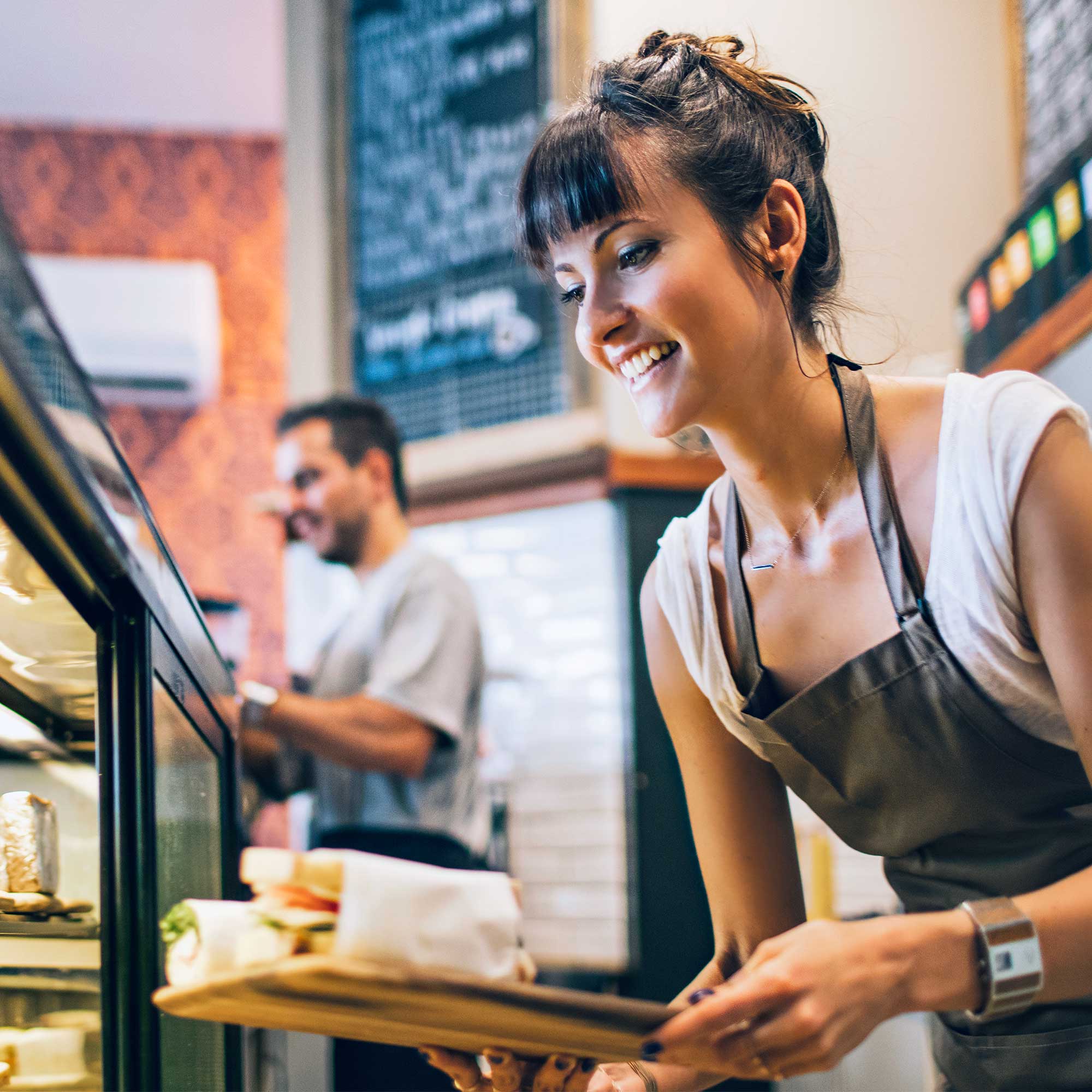 A woman wearing a white shirt and apron works behind the deli counter.